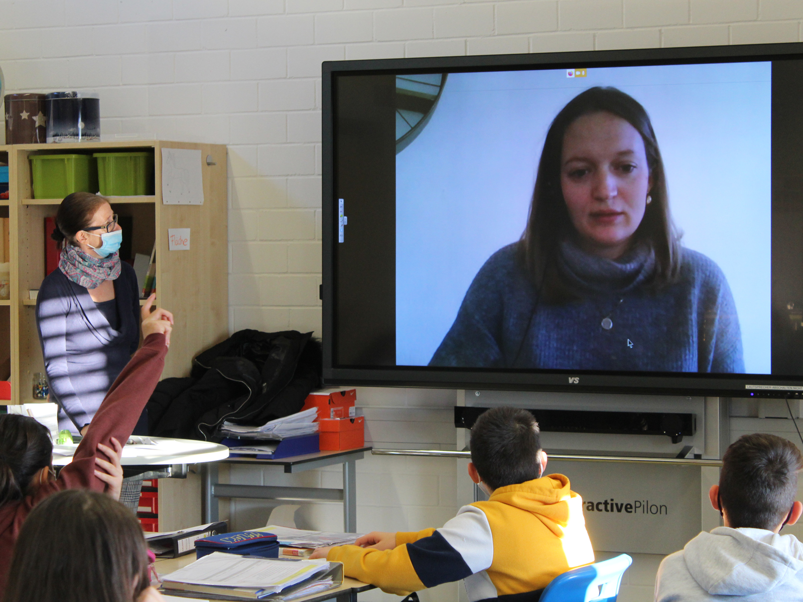  Lernbegleiterin Anna Mangold kommuniziert mit ihrer Klasse von zuhause über die Videokonferenz Talkie. Ihre Kollegin Stefanie Kreisl (links vorne) ist als Aufsichtsperson im Klassenzimmer. 